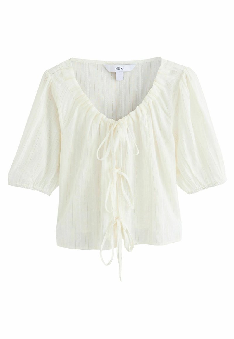 Blouse blanche texturée avec un décolleté en V profond, un devant noué et des manches courtes bouffantes. Présente des rayures verticales subtiles.