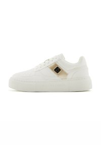 Zapatillas blancas de cuero sintético con una textura lisa, suela plana tipo plataforma, detalles en dorado y perforaciones en la zona de los dedos.