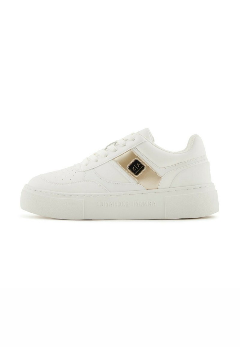 Zapatillas blancas de cuero sintético con una textura lisa, suela plana tipo plataforma, detalles en dorado y perforaciones en la zona de los dedos.