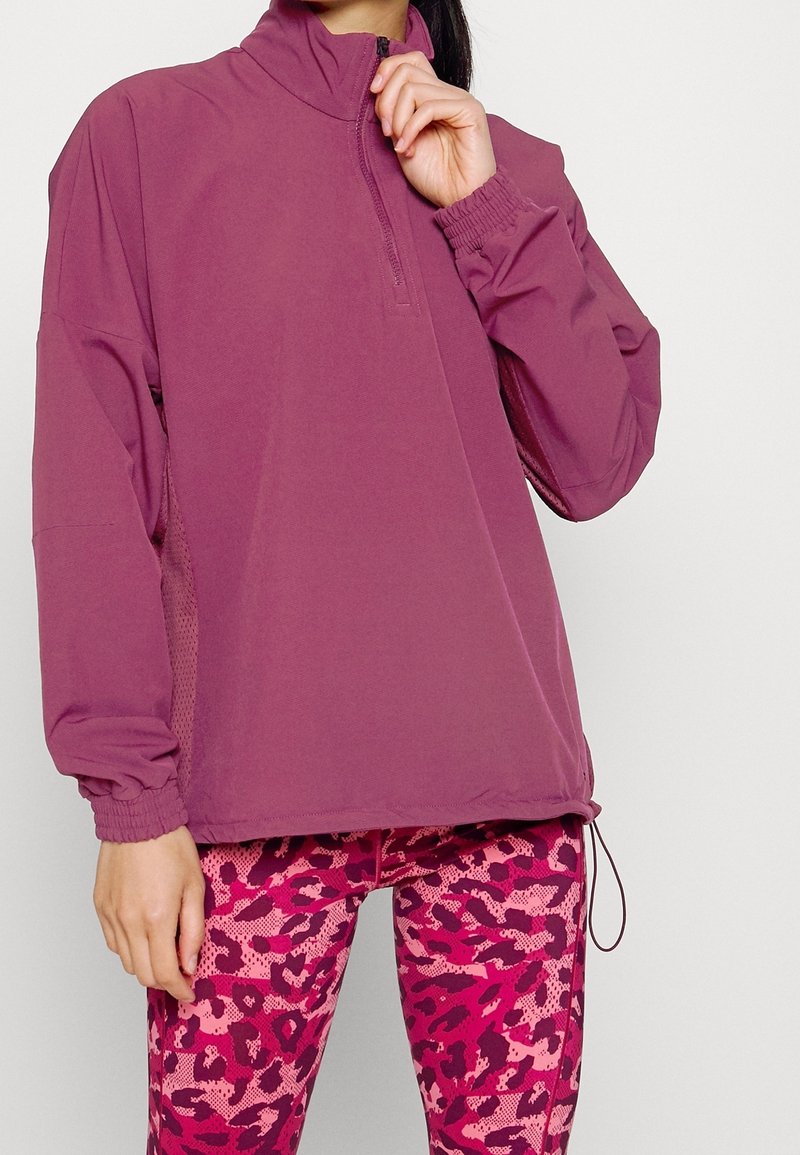 Sudadera morada con medio cierre y puños elásticos, combinada con leggings de estampado de leopardo rosa con patrones texturizados.
