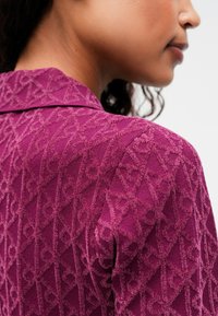 Õhukesest nyöörmaterjalist magenta värvi kudum, millel on rombikujuline ja silmuste muster, klassikalise krae ja sobiva lõikega.