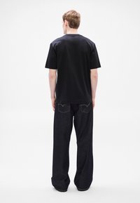 Fekete pamut rövid ujjú póló, laza szabású sötét farmernadrággal, finom varrással és hátsó zsebekkel.