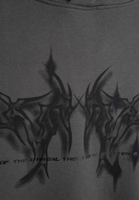 Szary sweatshirt z ciemnym, abstrakcyjnym wzorem graficznym z ostrymi kątami. Gładka tekstura z nadrukowanym tekstem w pobliżu dołu.