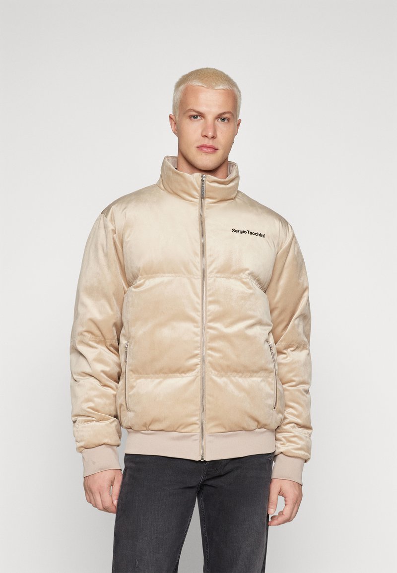 Giacca imbottita beige con collo alto, chiusura a zip e logo sul lato sinistro; realizzata in materiale morbido e testurizzato; polsini e orlo a coste.