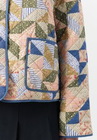 Giubbotto trapuntato con un design a patchwork di triangoli in verde, blu, rosa e motivi floreali. Rifinito con tessuto blu, include tasche.