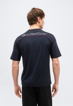 Άνδρας που φαίνεται από πίσω, φοράει μαύρο t-shirt Quiksilver με κοντά μανίκια και κόκκινη ραφή κατά μήκος των ραφών στους ώμους.