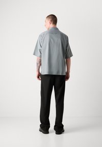Camisa gris de manga corta confeccionada en tejido ligero, con un corte recto. Pantalones negros de corte relajado, combinados con zapatos negros resistentes.