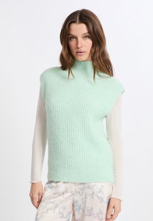 Maglione senza maniche color verde menta con un motivo a maglia testurizzata. Indossato sopra una leggera maglietta a maniche lunghe, abbinato a pantaloni del pigiama con motivo.