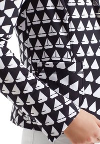 Chaqueta negra con un patrón de veleros blancos, que presenta un corte ajustado, tejido texturizado y un bolsillo de mano en el lado frontal.