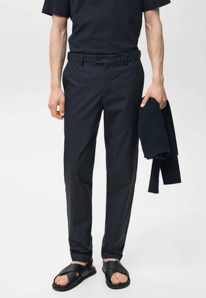 Marineblaue, leichte Hose mit taillierter Passform, flachem Bund und seitlichen Taschen, kombiniert mit einem passenden Strickoberteil und schwarzen Rutsch-Sandalen.