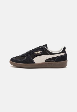 Sneaker nera in suede e tessuto con una striscia PUMA crema, suola in gomma e lacci neri. Cuciture dettagliate e accenti di branding.