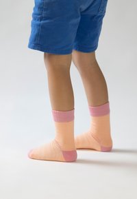Rosa og ferskenfarvede sokker med ribbet rosa manchetter, der har et stribet mønster og en glat tekstur, iført med blå shorts.