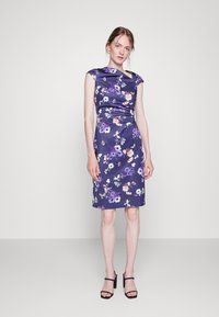 Vestido floral roxo em tecido de cetim, com um design ajustado, mangas curtas e uma bainha até ao joelho. Usado com sandálias de salto alto pretas.