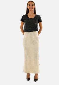 Top a maniche corte a righe bianche e nere abbinato a una gonna maxi beige a costine. L'outfit presenta una silhouette aderente e una texture liscia.
