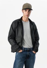 Black bomber jacket with a zip front, two front pockets, and a contrasting collar, worn over a gray t-shirt and blue jeans; a checkered cap.
