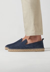 Zapatos azul marino de ante sin cordones con suela de cuerda de yute y diseño con recortes, presentando una parte delantera plana y un upper texturizado.