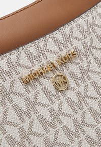 Sac blanc et beige présentant un motif texturé, des accessoires en or, et le logo "Michael Kors" affiché en lettres dorées.