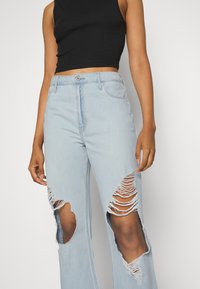 Jeans rasgados de azul claro com grandes cortes no joelho desfiados, design de cintura alta e estilo de cinco bolsos. Feitos de denim com uma textura suave.