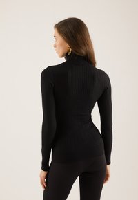 Svart ribbet turtleneck genser med lange ermer og en tettsittende design, med et teksturert mønster og høy hals.