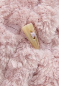 Blød lyserød, fluffy stof med en beige toggle-knap sikret af en matchende lyserød snor, der går igennem den.