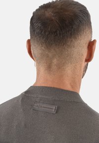 Maglione grigio a maglia con scollo rotondo, che mostra una superficie testurizzata e una piccola etichetta sulla parte posteriore del collo. Inquadratura ravvicinata da dietro.