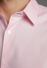 Helles rosa Button-Up-Hemd mit Kragen, das eine glatte Textur, weiße Knöpfe und ein dezentes Streifenmuster in der Nähe des Kragens aufweist.