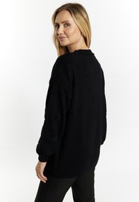 Maglione nero oversize con maniche texturizzate e polsi a coste, caratterizzato da un design con collo rotondo e una vestibilità rilassata, abbinato a pantaloni neri.