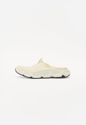 Zapatilla de malla color crema sin cordones, con una suela blanca gruesa y una suela exterior texturizada negra. Presenta una lengüeta en el talón para facilitar su uso.