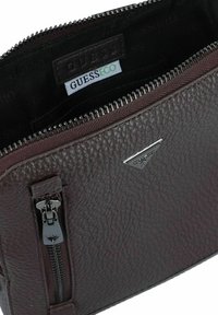 Borsa in pelle testurizzata di un profondo bordeaux scuro con una zip argentata, caratterizzata da un piccolo accento metallico del logo e un interno foderato con etichetta del marchio.