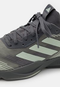 Šedá sportovní bota s texturovaným síťovaným svrškem, nastavitelným šněrovacím systémem a světle zelenými akcenty, s zakřivenou, polstrovanou podrážkou.