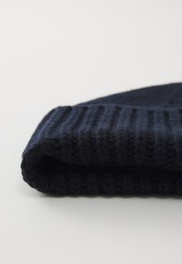 Berretto lavorato a maglia di un blu navy scuro con una texture a coste. Il tessuto sembra morbido e presenta un orlo spesso nella parte inferiore.