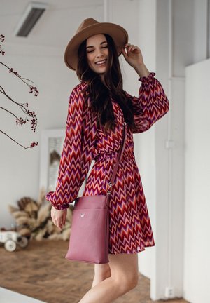 Mehrfarbiges Kleid mit Zickzackmuster in Rot, Pink und Lila, mit Puffärmeln, kombiniert mit einer einfarbigen burgunderroten Umhängetasche.