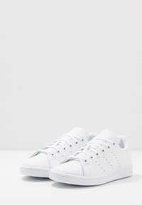 Vita lädersneakers med rund tå, perforerade sidor och platta snören. Har en texturerad gummisula och logotyp på sidan.