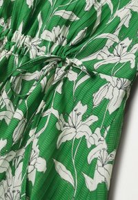 Grünes Blumenkleid mit einem weißen Lilienmuster, leichtem Stoff, gerafft an der Taille mit Kordelzug und dezentem Texturmuster.