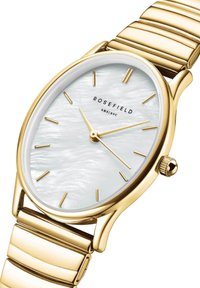 Zlatni sat s okruglim brojčanikom koji ima završnu obradu od bisernog materijala, minimalističke oznake za sate i metalnu narukvicu s povezanim člancima.