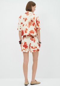 Korte mouwen shirt met cropped model en bijpassende shorts in crèmekleur met rode bloemenprint. Zachte stof, losse pasvorm, zichtbare stiksels.