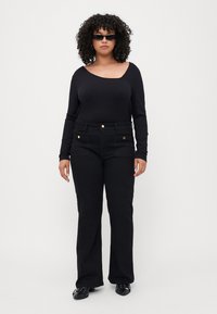 Black ribbed long-sleeve top with a wide neckline, paired with black flared pants featuring front pockets and gold button accents.