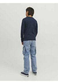 Navy long-sleeve shirt paired with light blue cargo jeans featuring side pockets. Sneakers with a white sole complete the outfit.