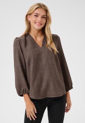 Blouse marron, texturée, à col en V avec de longues manches ballon, présentant une coupe décontractée et des poignets élastiques, associée à un pantalon noir.