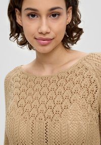 Beige Strickpullover mit strukturiertem Muster. Das Design zeichnet sich durch einen weiten Ausschnitt und filigranen Spitzenarbeiten aus, die die dezenten Details betonen.