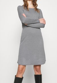 Langärmliges Kleid in Schwarz und Weiß mit geometrischem Muster. Gerade geschnitten, aus weichem Stoff, knielang, mit rundem Ausschnitt.