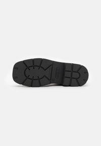 Suola di scarpa nera in gomma con un motivo di battistrada testurizzato e scanalature. Contrassegnata con "GUESS" e di misura 46, progettata per aderenza e durata.