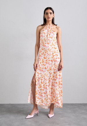 Floral maxi dress in light fabric with orange and pink patterns, halter neckline, side slit, and paired with pink heeled mules.