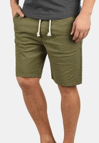 Pantalones cortos de color verde oliva hechos de una tela ligera, con una cinturilla elástica con cordones blancos, parte delantera plana y bolsillos laterales.