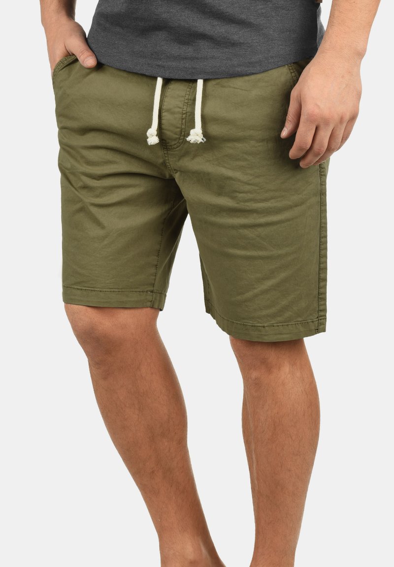 Pantalones cortos de color verde oliva hechos de una tela ligera, con una cinturilla elástica con cordones blancos, parte delantera plana y bolsillos laterales.