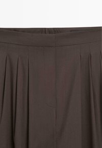 Jupe plissée marron avec une ceinture lisse et une fermeture avant dissimulée.