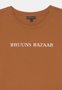 T-shirt castanho feito de tecido macio, com decote redondo e texto em branco em relevo a dizer "BRUUNS BAZAAR" no peito. Etiqueta de tamanho 12.