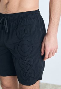Shorts de bain noirs avec taille élastique et cordon de serrage, logo "BOSS" en relief sur le côté et tissu léger texturé.