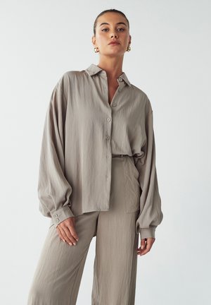 Light gray, oversized button-up shirt with a soft texture, long sleeves, a collar, and subtle sheen, paired with matching loose trousers.