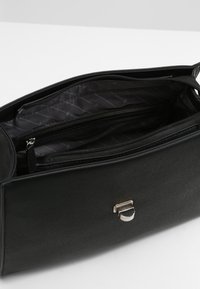 Sac à main en cuir noir avec une surface texturée, doté d'une fermeture éclair et de quincaillerie en argent. L'intérieur possède plusieurs compartiments en doublure en tissu noir.